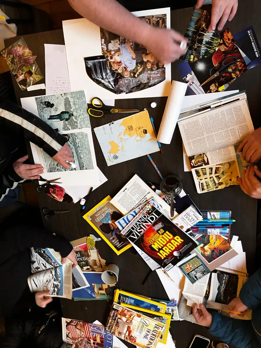 An overhead photograph of the Mental Bytes workshop table, with hands making collages among magazines, coloured paper, scissors and drawing materials